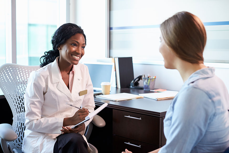 A healthcare professional at her desk takes information from a patient